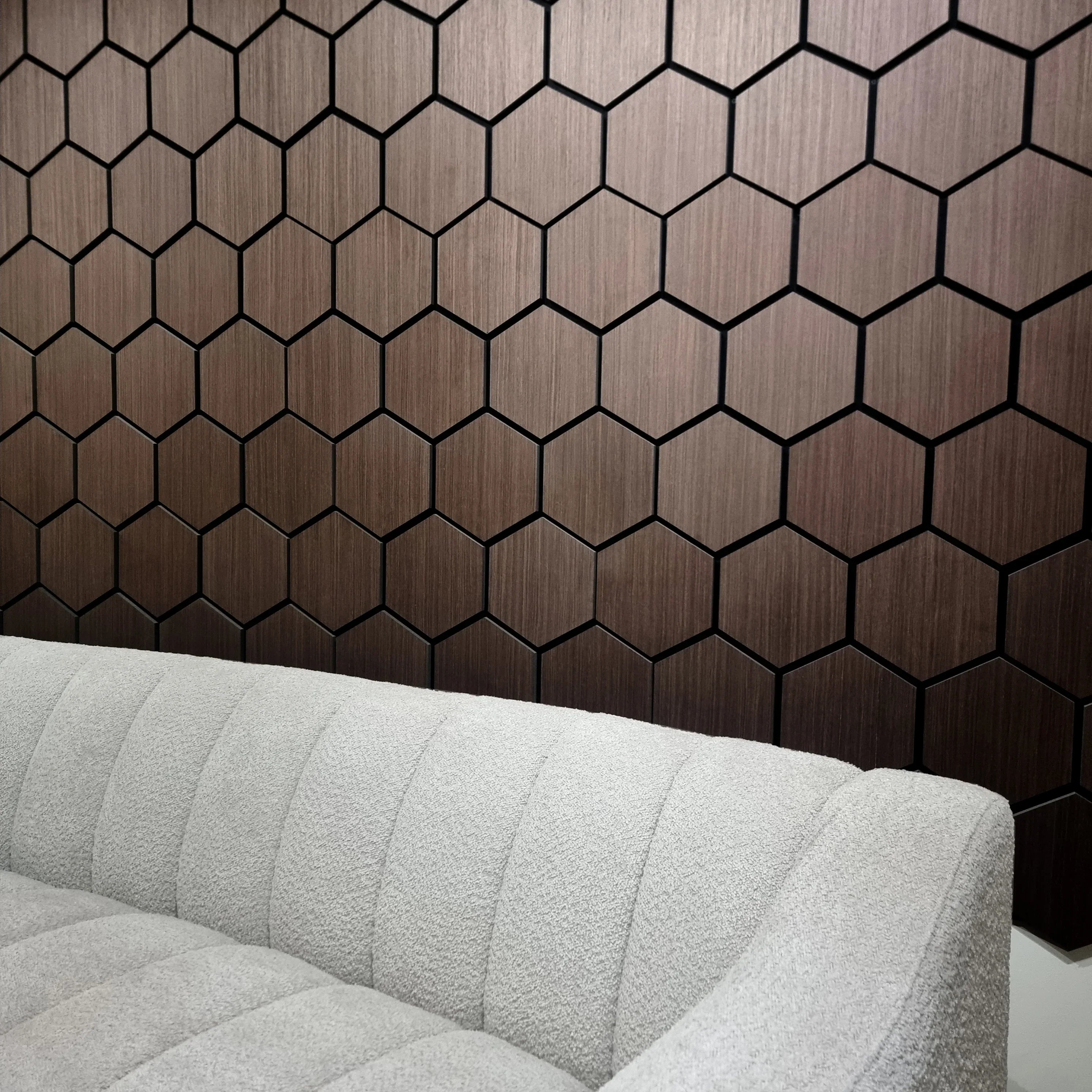 Hexagonal wooden panel wall with a gray sofa in front
