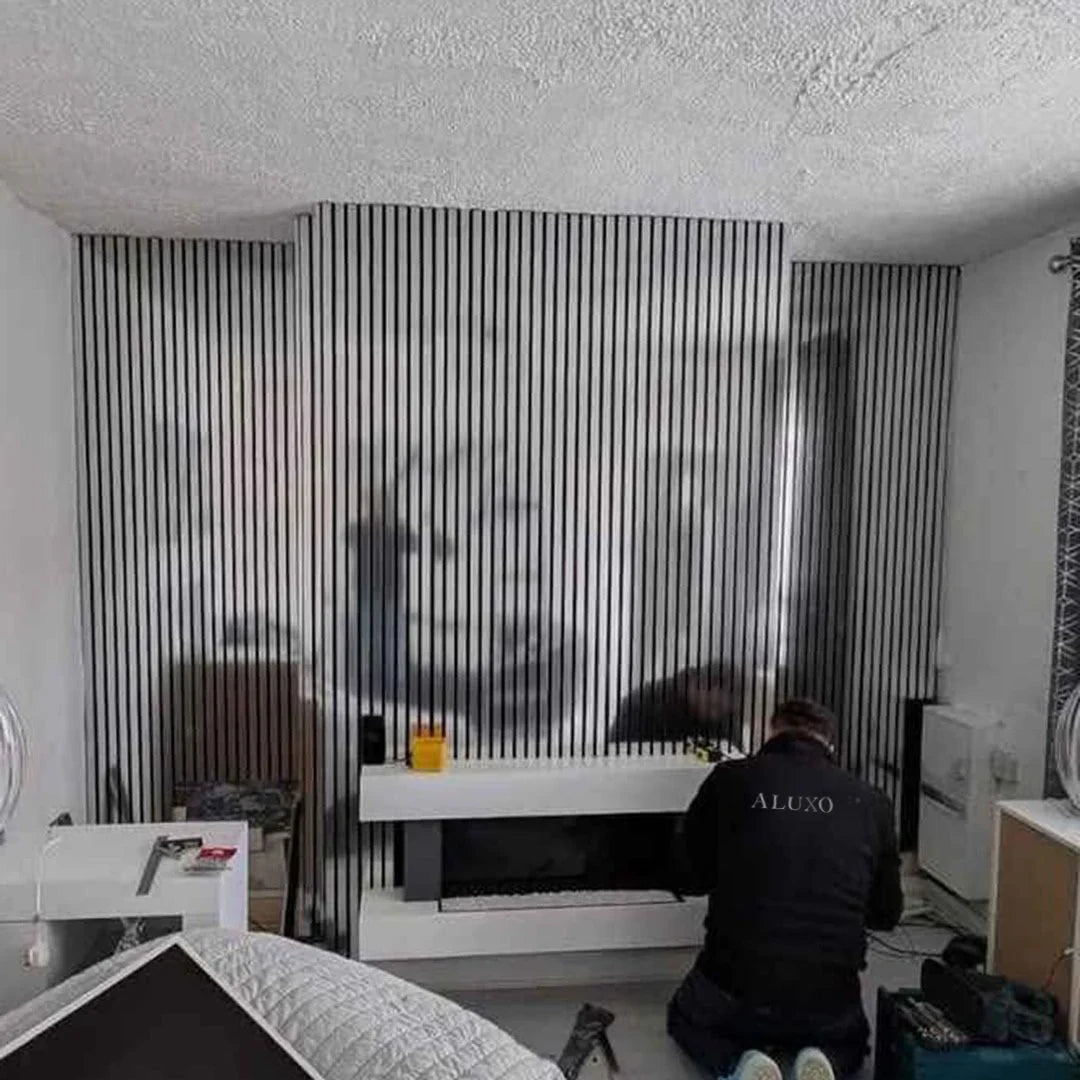Person working on a modern fireplace setup in a room with striped wall design.