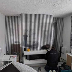 Person working on a modern fireplace setup in a room with striped wall design.
